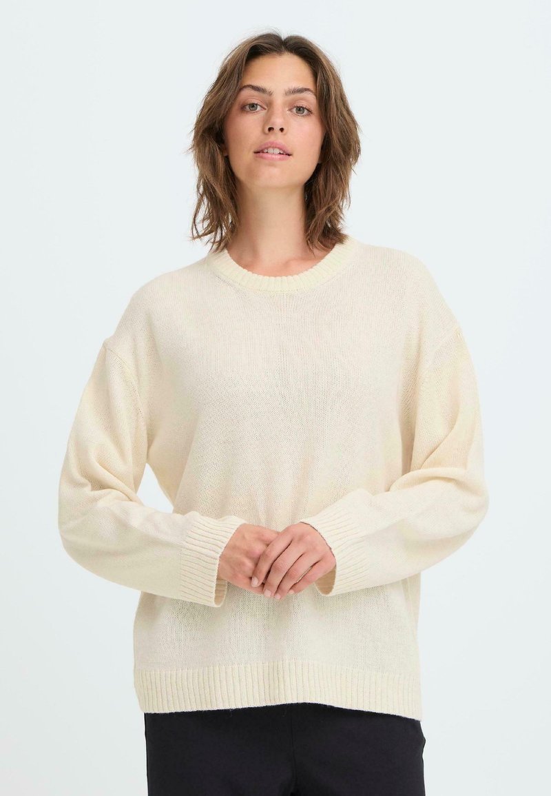 Ljusbeige stickad tröja med rund halsringning, nedfallna axlar och ribbade muddarn. Mjuk textur med en avslappnad passform.