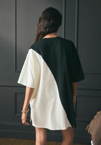 Oversized t-shirt w czarnym i kremowym kolorze z bawełny, z ukośnym wzorem bloków kolorów. Krótkie rękawy i okrągły dekolt.