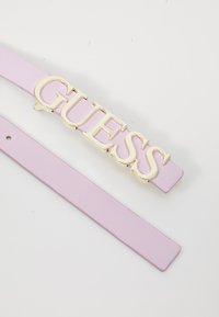 Lila Leder-Gürtel mit einer großen goldenen "GUESS"-Logo-Buckle. Der Riemen ist glatt und hat eine klassische rechteckige Form.