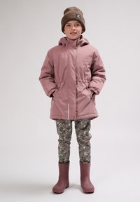 Roze waterdichte jas met capuchon, elastische taille, en zijzakken, gecombineerd met gestreepte groene leggings en roze rubberen laarzen.