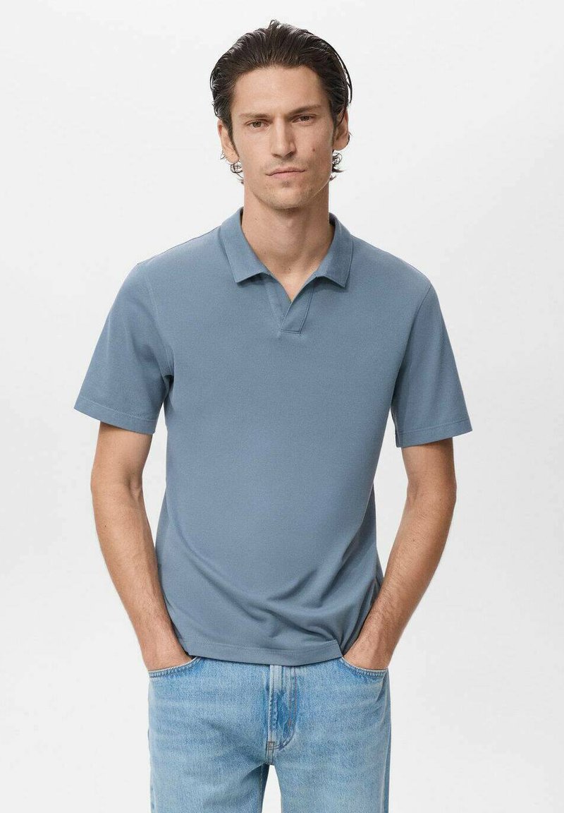 Polo de tela azul suave, con cuello y mangas cortas. El diseño es sencillo, con un corte recto, combinado con jeans de un azul claro.