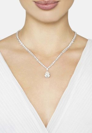 Silver-tone necklace featuring pear-shaped clear pendant, surrounded by sparkling crystal accents, worn against a white fabric background.