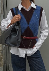 Chaleco de lana azul y burdeos con patrones de rombos sobre una camisa blanca, combinado con jeans de mezclilla oscura y un bolso de hombro de cuero negro.