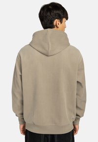 Sudadera beige con textura acanalada, una capucha amplia y corte relajado. Presenta hombros caídos y un dobladillo acanalado para mayor comodidad.