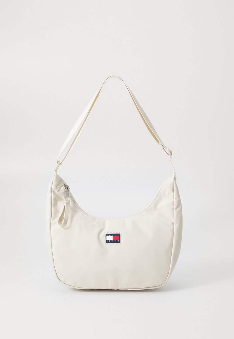 Bolsa de ombro branca em nylon com um design curvado, apresentando um patch com logotipo, detalhe de fecho éclair e uma textura suave e macia. Inclui alça ajustável.