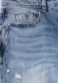 Svetle modré denimové džíny s roztrženou nášivkou a malou přední kapsou. Tkanina má jemnou strukturu a kontrastní prošití.