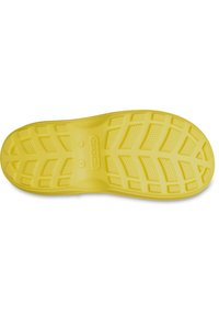 Yellow Crocs shoe sole with textured tread pattern and brand name embossed in the center, shown from the bottom.