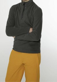 Ciemnoszary polar z zamkiem i stojącym kołnierzem, z dyskretnym logo i długimi rękawami, zestawiony z jaskrawożółtymi spodniami.