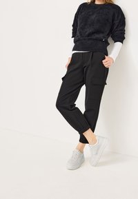 Black cargo joggers with elasticated cuffs, featuring two side pockets. Paired with a loose black fuzzy sweater and white sneakers.