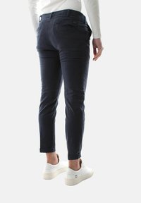 Chinos blu scuro con una vestibilità slim, dotati di tasche posteriori e risvolti. Abbinati a scarpe da ginnastica bianche, per un look casual.