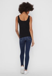 Black tank top with a scoop back, paired with dark blue skinny jeans, and white sneakers. The tank has a fitted design and smooth texture.