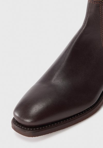 Botine din piele maro, cu vârful ascuțit, textură netedă și detalii de cusătură în contrast pe laterală și talpă.
