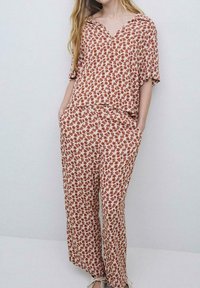 Blomster loungewear sæt bestående af en kortærmet top og løse bukser, i krem med røde og brune blomstermønstre, lavet af let væv.