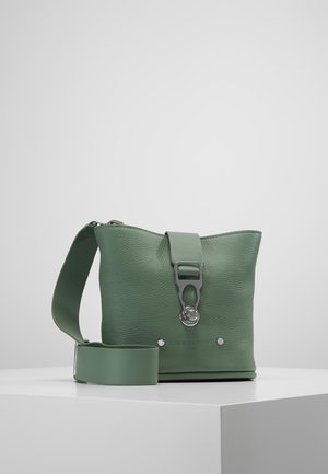Sac bandoulière en cuir vert texturé avec une large sangle réglable et une boucle en métal argenté, présenté sur un socle blanc contre un fond uni.