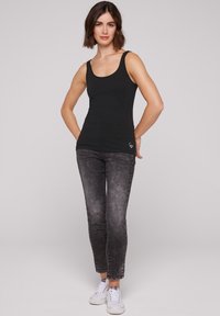 Top sin mangas negro combinado con jeans desgastados negros y zapatillas blancas. El top es ajustado, con escote redondeado y detalle de logo.