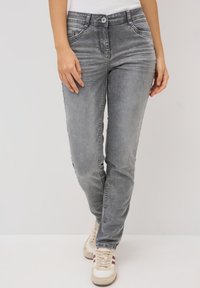 Grijze spijkerbroek met een nauwsluitend ontwerp, voorzien van vijf zakken, een knoopsluiting en een lichte vervaging voor textuur. G gedragen met beige sneakers.