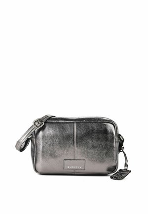 Bolso bandolera metálico pequeño y rectangular en plata con correa ajustable y etiqueta frontal con el texto "BURKELY" sobre fondo blanco.