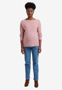 Rosa gestrickter Pullover mit einem Bootauschnitt, strukturiertem Muster und langen Ärmeln, kombiniert mit blauen Jeans und braunen Stiefeletten.