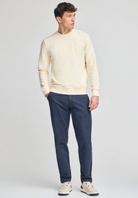 Sweatshirt giallo chiaro con testo in rilievo "POLO CLUB", abbinato a pantaloni blu navy e sneaker color crema. Tessuto liscio, vestibilità casual.