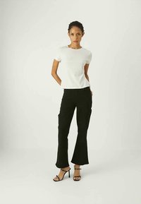 Top bianco a maniche corte abbinato a pantaloni neri a palazzo. Tessuto trasparente per il top, finitura liscia per i pantaloni. Tacchi a stiletto completano l'outfit.
