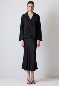 Blusa nera floreale con scollatura a V e maniche lunghe, abbinata a una gonna midi nera aderente. Cinghie sottili su tacchi neri. Accenti di gioielli semplici.