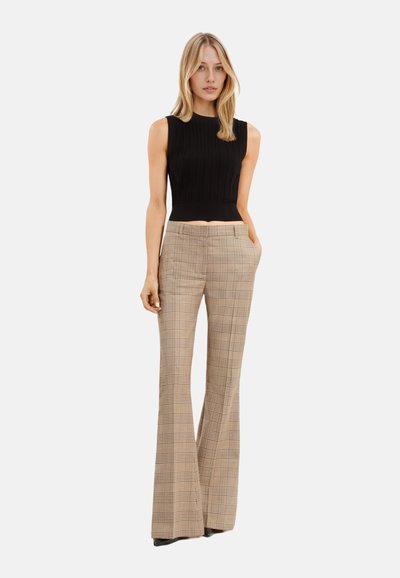 Un crop top noir à côtes associé à un pantalon évasé à carreaux beige, avec poches et taille haute.