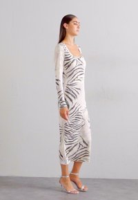 Šaty s dlhým rukávom v pruhovanom vzore zebra v krémovej a čiernej farbe, s priliehavým strihom a výstrihom s okrúhlym výstrihom. Číre sandále na podpätku dotvárajú vzhľad.