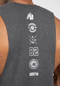 Grijze mouwloze tanktop met witte bedrukte graphics, waaronder logo's, de tekst "Gorilla Wear" en het nummer "82" op de achterkant.