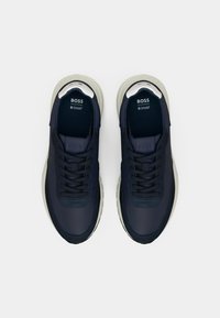 Ναυτικά αθλητικά παπούτσια με λείο συνθετικό επάνω μέρος, σχέδιο με κορδόνια, αντίθετη κρεμ σόλα και εμφανές λογότυπο στη γλώσσα.