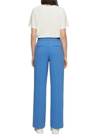 Pantaloni blu a gamba larga con una trama liscia, dotati di due tasche posteriori, abbinati a una maglietta bianca semplice e a sneaker bianche.