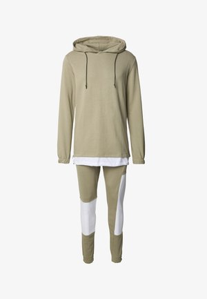 Kapuzensweatshirt in hellem Olivgrün mit schwarzen Kordeln, kombiniert mit engen, olivgrünen Leggings mit weißen Einsätzen. Hergestellt aus Baumwollmischgewebe.