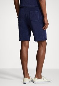 Mörkblå frottéshorts med elastisk midja och bakficka, med rak passform och fållade cuffs. Avslappnad design.