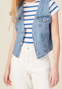 Jasnoniebieska kamizelka dżinsowa z srebrnymi zatrzaskami, o kroju krótkim, z dwiema kieszeniami na piersi i przetarciami, zestawiona z paskowanym topem.
