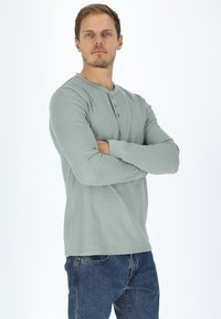 Vihreä raidoitettu pitkähihaine paita, jossa on pyöreä kaula-aukko ja kolme napin aukkoa. Yhdistetty sinisiin farkkuihin.