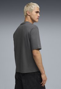 Camiseta de algodón gris con mangas cortas, escote redondo, corte relajado y detalles de costura mínimos, combinada con jeans negros.