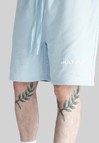 Světle modré bavlněné kraťasy s nastavovací šňůrkou v pase a slovem "MULTIPLY" bílé barvy na levé nohavici. Na lýtkách se nacházejí zelené tetování listů.