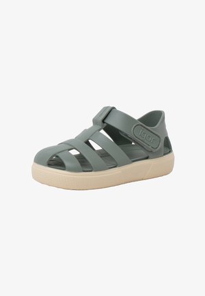 Green rubber sandal with open design, adjustable strap, and cream-colored sole featuring a textured surface and branding on the strap.