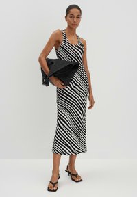 Schwarz-weißer gestreifter Midi-Kleid mit ärmellosem Design, Rundhalsausschnitt und figurbetontem Schnitt. Das Modell hält eine strukturierte schwarze Tasche.