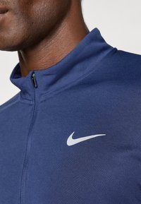 Αθλητική ζακέτα Nike με φερμουάρ σε ναυτικό μπλε χρώμα, με λεία και αναπνεύσιμη υφή. Διαθέτει ψηλό γιακά και λευκό λογότυπο στη αριστερή πλευρά.
