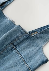Džínové overaly vo svetlom modrom odtieni, s nastaviteľnými ramienkami, rovnými nohavicami a viditeľným šitím. Mäkká textura s vyblednutým povrchom.