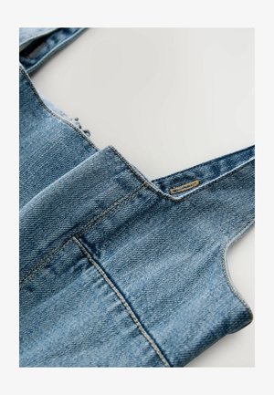 Heled sinine denim ülekoode, millel on reguleeritavad rihmad, sirged sääred ja nähtav õmblus. Pehme tekstuur ja pleekinud viimistlus.