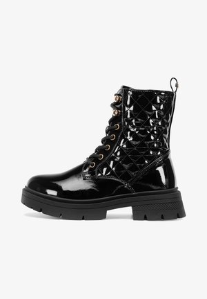 Melns spīdīgs kaujas zābaks ar dūrienu izšūtu augšējo daļu, zelta acīm, biezu protektora zoli un cilpu aizmugurē, redzams sānu profilā.