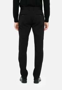 Schwarze Hose mit schmaler Passform, ausgestattet mit zwei Gesäßtaschen, dezenten Nähdetails und einer glatten Stofftextur.
