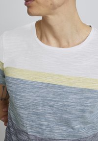 Camiseta de manga corta con cuello redondo, que presenta rayas horizontales en blanco, amarillo, azul y gris, con una tela texturizada.