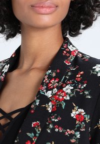 Květinové černé sako s výraznými červenými a bílými květy, výstřihem se zářezem, lehkou látkou a zvýrazněné texturovaným povrchem.