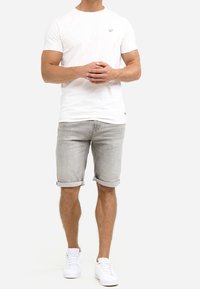 Witte t-shirt met korte mouwen en klein logo, gecombineerd met lichtgrijze denim shorts omgeslagen aan de zoom, afgewerkt met witte sneakers.
