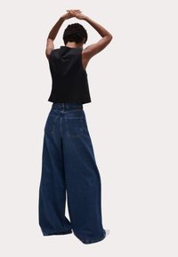 Top negro sin mangas combinado con jeans de mezclilla oscuros de pierna ancha, con bolsillos traseros y cintura alta. Modelo de espaldas, con los brazos levantados.