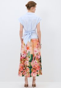 Vaaleansininen lyhythihainen paita, jossa on sidottava yksityiskohta takana, yhdistettynä kukallisiin midi-hameisiin, joissa on vaaleanpunaisia ja vihreitä sävyjä.