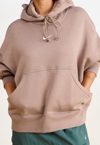 Przewymiarowana beżowa bluza z miękkiego materiału z przednią kieszenią, regulowanym kapturem ze sznurkiem i haftowanym białym logo Nike.