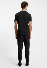 Czarna koszulka polo z wzorzystym kołnierzykiem, z krótkimi rękawami z szarymi akcentami. Do tego czarne, dopasowane spodnie i czarne buty.